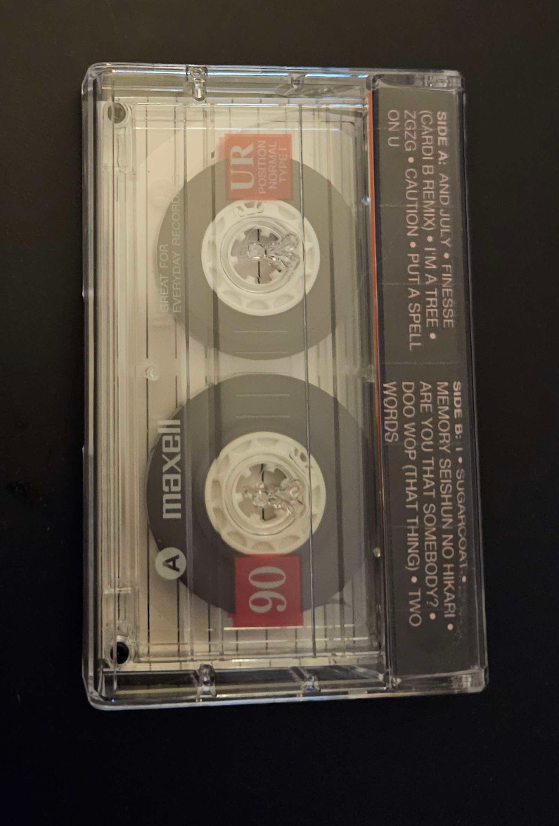 my physical recorded tape for the above playlist in a case with a custom j-card, but taken from the back of the case, and the case is clear so the cassette tape inside is visible