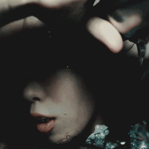 XG music video gif of cocona shaving her head in a room where the lights are flashing and flickering