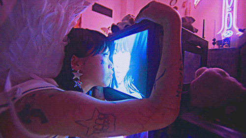 shot from the ARTMS virtual angel music video in which a girl adorned in ARTMS iconography presses her face to a CRT television with choerry's face on it as choerry sings