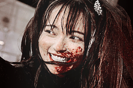 GIF of lachesis from kamen rider gotchard in her TTFC special. she's looking to the side off camera and smiling and laughing wildly with half of her face splattered with blood