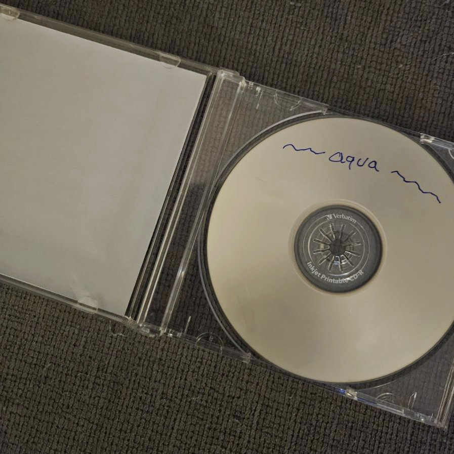 my physical burned CD for this mix in a jewel case, which is open to show the disc inside that has text written in blue marker ink that reads 'aqua' with swirls beside the word