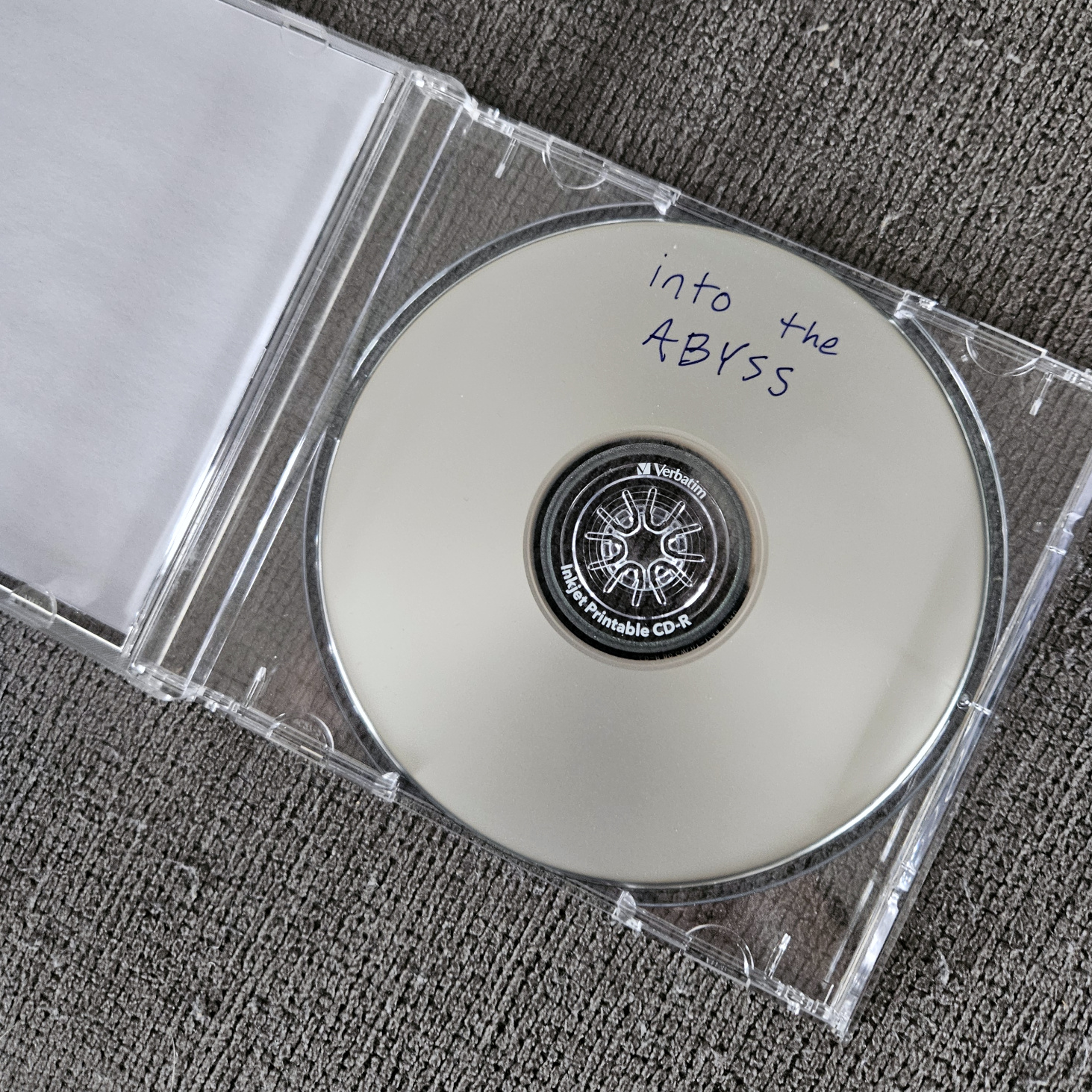 my physical burned CD for this mix in a jewel case, which is open to show the disc inside that has text written in blue marker ink that reads 'into the abyss'