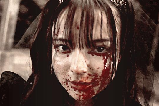 GIF of lachesis from kamen rider gotchard in her TTFC special. she's looking straight into the camera and smiling ominously, still with blood all over her face