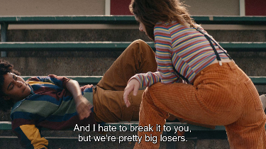 still from the movie 'bottoms' from 2023 where PJ leans over josie, who is stretched out on high school bleachers, and says 'and i hate to break it to you, but we're pretty big losers'