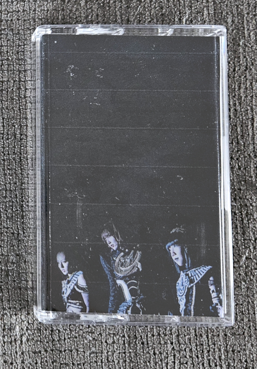 my physical recorded tape for the below playlist in a case with a custom j-card showing the cover art, which is an edit of the abyssalis sisters from kamen rider gotchard standing about to jump into action, the cover is very dark and mildly cool toned with a distortion texture applied and most of the background of the original image faded out into a cool toned black, and then there's a list of the tracks