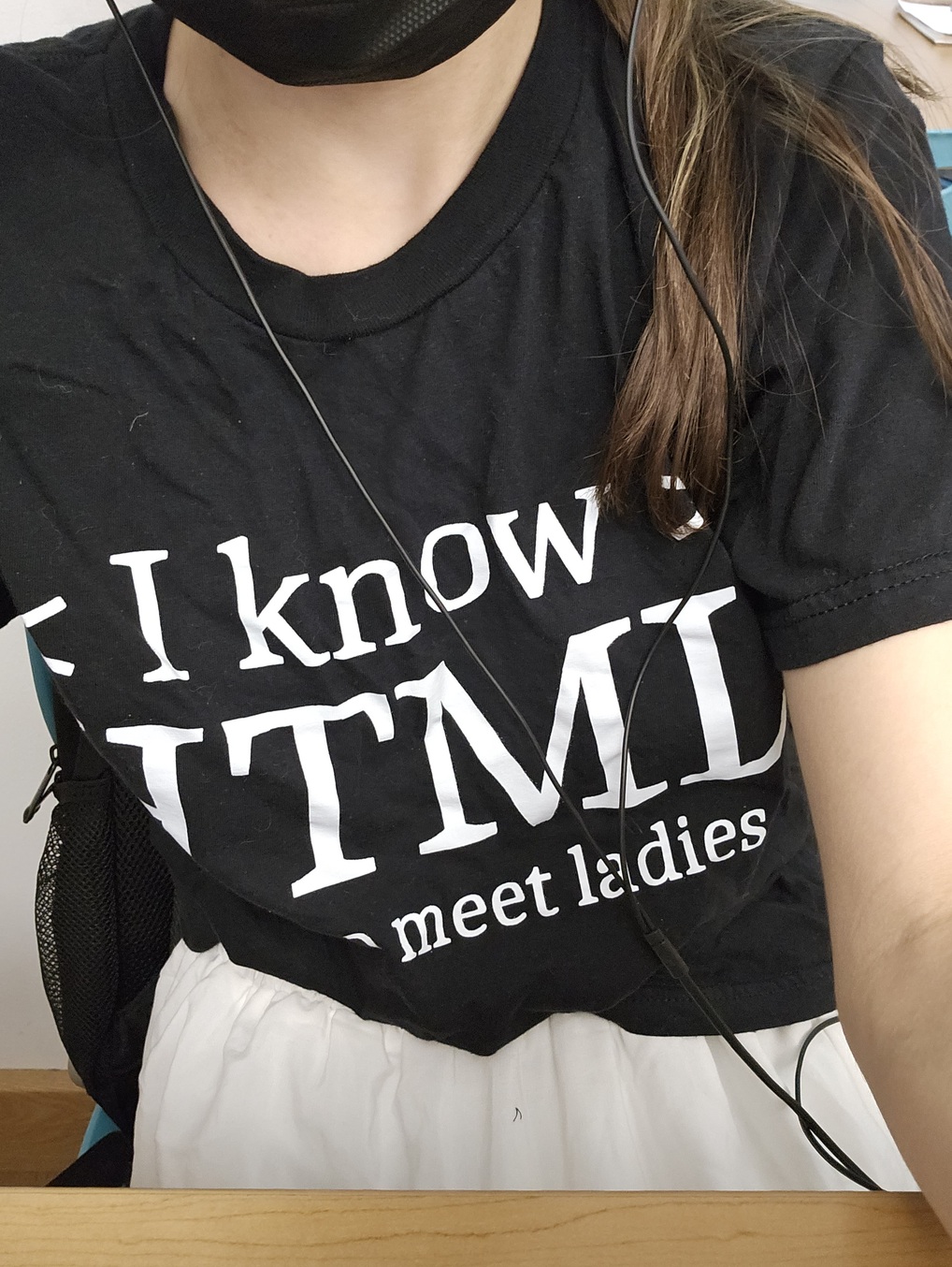 selfie of me from the face down (my face is covered with a black surgical mask). my t-shirt is visible but a little wrinkled because i'm sitting; it says 'I know HTML: how to meet ladies'