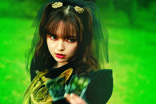 GIF of lachesis in kamen rider gotchard raising her hand which holds two chemy cards between her fingers. the GIF is highly saturated with the green tones emphasized and highlighted