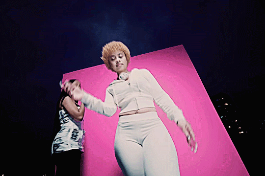 ice spice with pink pantheress in their music video for boy's a liar part 2. she raps in the foreground, leaning in and grabbing the camera, while pink dances in the background on the rooftop set