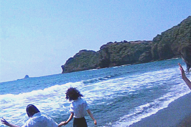 new jeans bubble gum music video screen shot showing the members playing around on a beach. the image is sharpened with the lighting and colors shifted