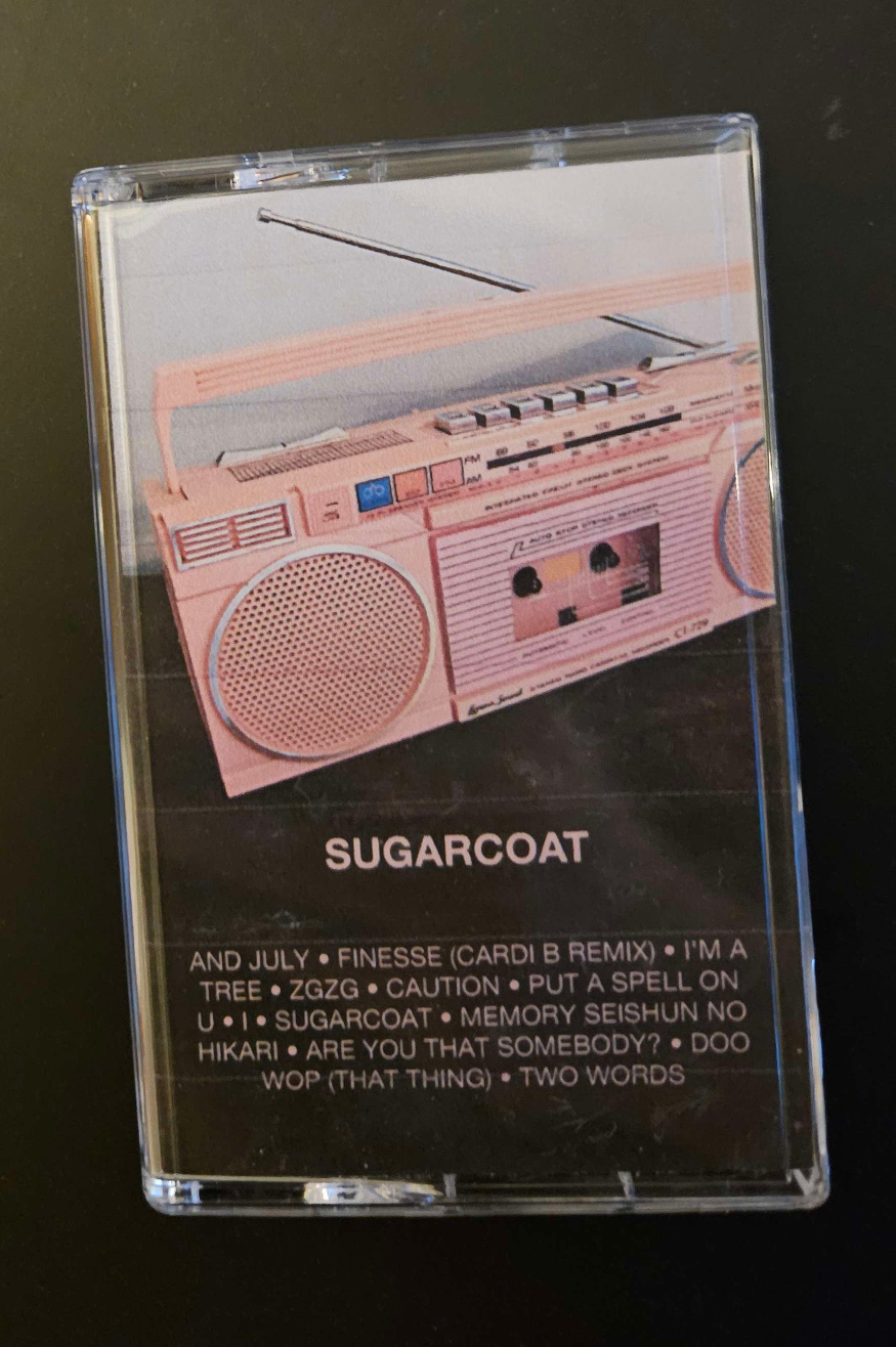my physical recorded tape for the above playlist in a case with a custom j-card showing the cover art, which is a pink 1990s boombox with a built in cassette player, and a list of the tracks