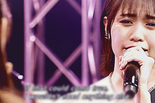 the camera is over oda sakura's shoulder, focusing on sayuki, as she sings with sakura