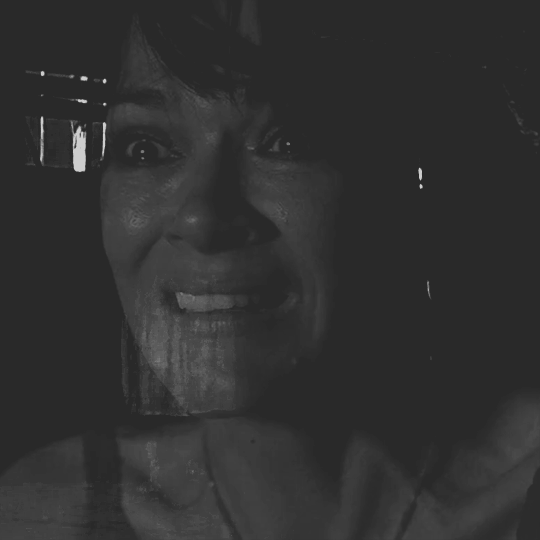 two black and white GIFs layered on top of each other. the first one is lottie's hallucination of laura lee ominously stepping forward, engulfed in shadow. the second one is adult lottie staring at the vision in horror with tears in her eyes