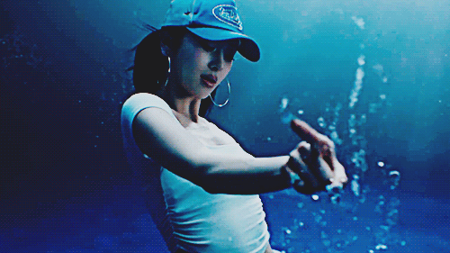 yunjin in the le sserafim crazy music video wearing a cool outfit in a blue background underwater kinda scene swirling around her finger in the air and water moves with it