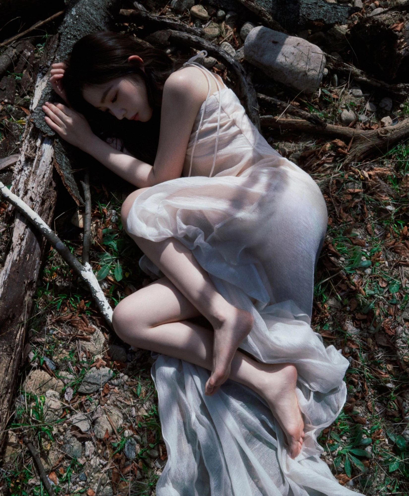 irene from red velvet in a white dress curled up and resting or sleeping on the ground, clutching the roots of a tree